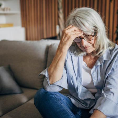 Retirement-age woman sitting on a couch looking worried while reviewing finances, representing concerns about creating lifetime income for a surviving spouse.