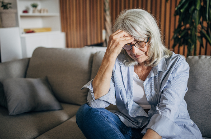 Retirement-age woman sitting on a couch looking worried while reviewing finances, representing concerns about creating lifetime income for a surviving spouse.