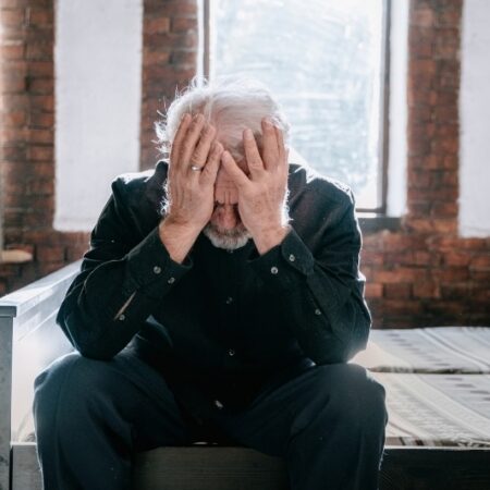 Retired man sitting on bed with hands on his head looking stressed, representing regret and common mistakes retirees make when buying annuities